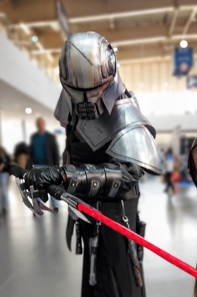 Cosplayer in Starkiller's armoured helmet with a red lightsaber at Poznań Game Arena 2021